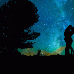 A whimsical image of the silhouette of a man and woman embracing. There is a silhouette of a tree on their left and stars and the moon light in the background.